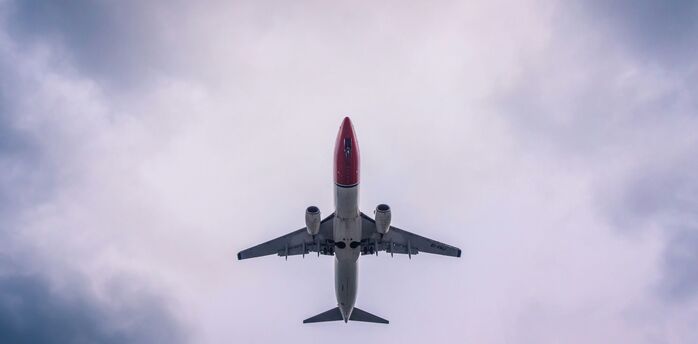 A Norwegian Air aircraft flying overhead against a cloudy sky