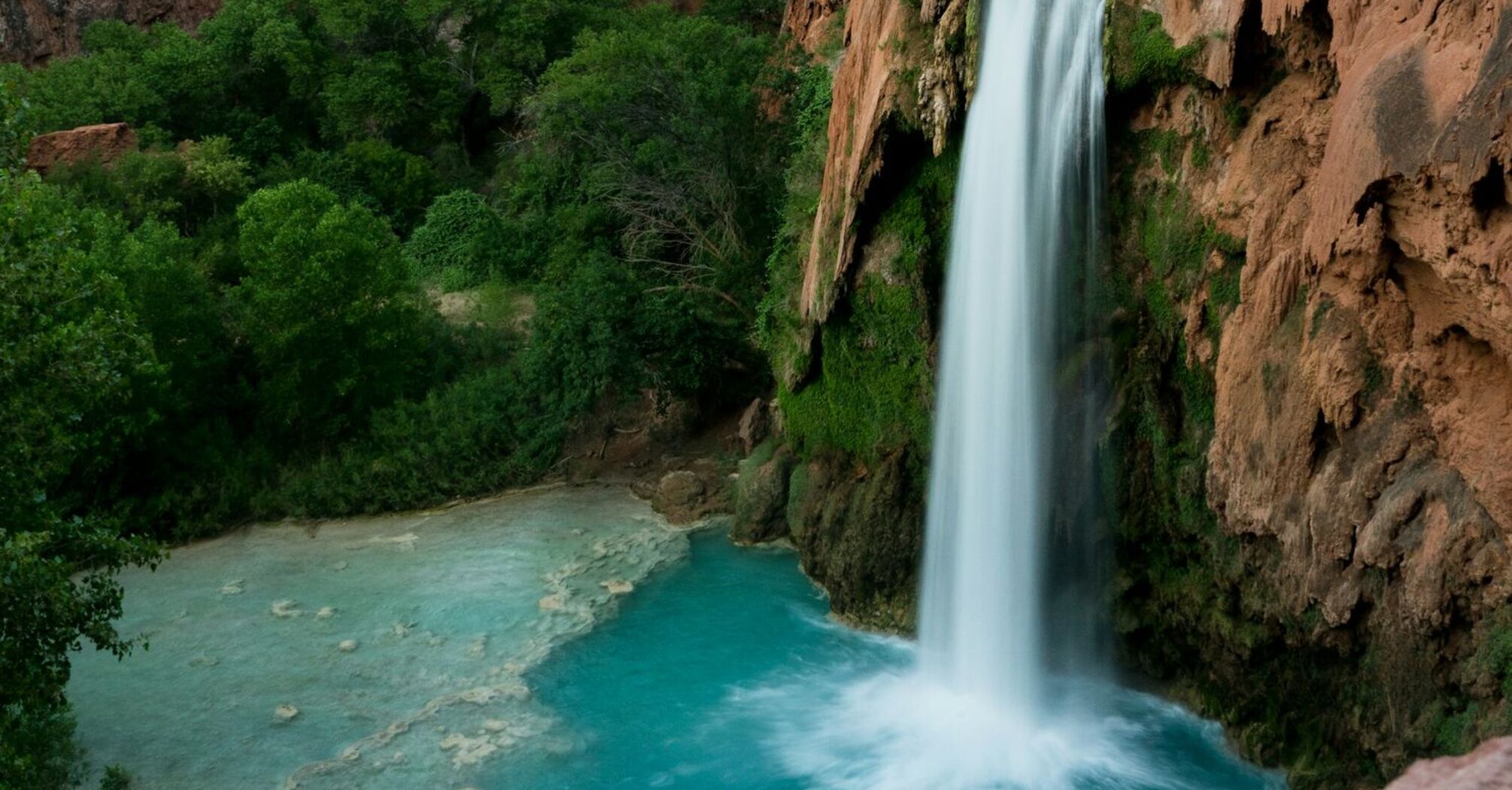 Scenic view of Havasu Falls cascading into a turquoise pool surrounded by towering red cliffs and lush greenery