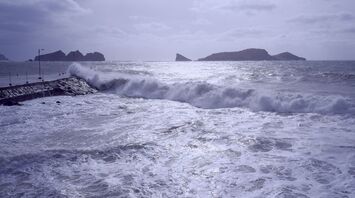Waves crashing against a pier with distant islands in the background during a stormy sea