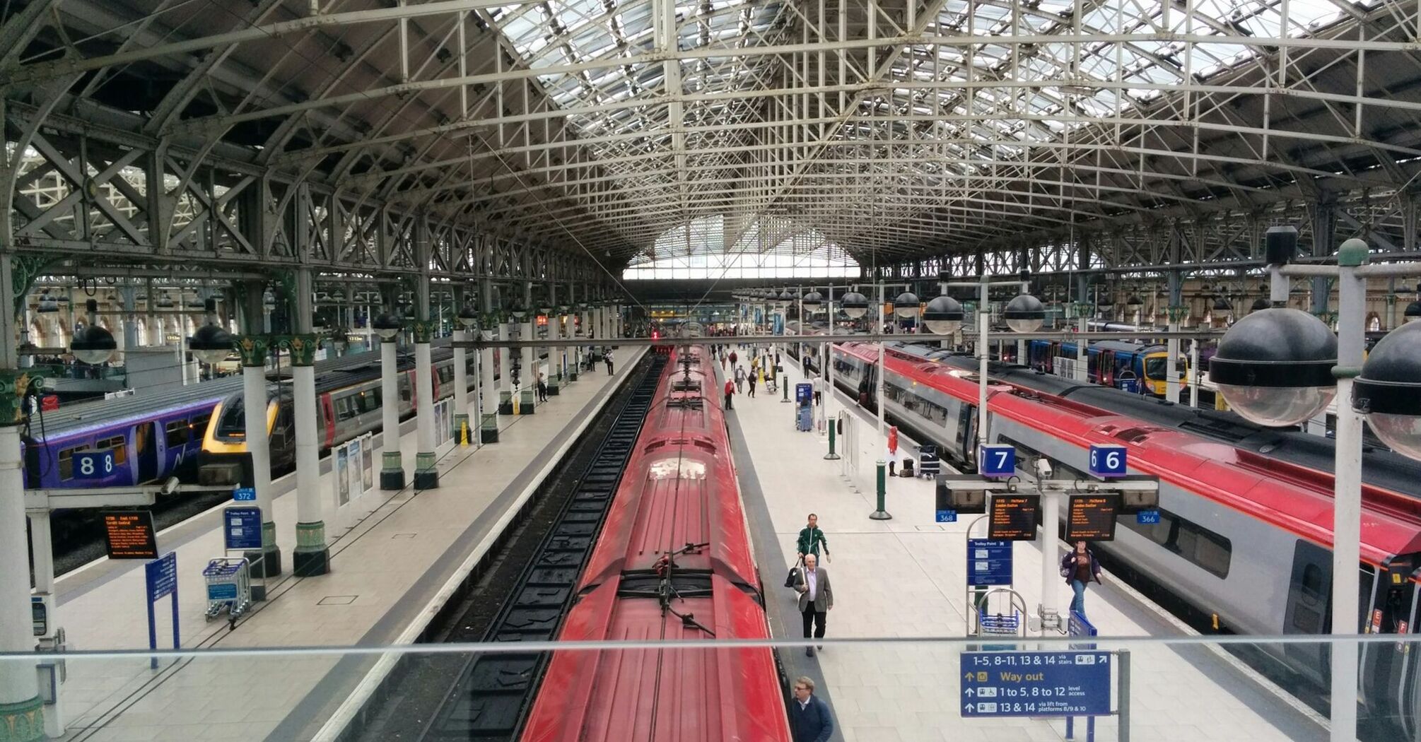 A view of Piccadilly Station with multiple platforms, trains, and passengers, featuring the iconic glass roof