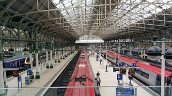 A view of Piccadilly Station with multiple platforms, trains, and passengers, featuring the iconic glass roof