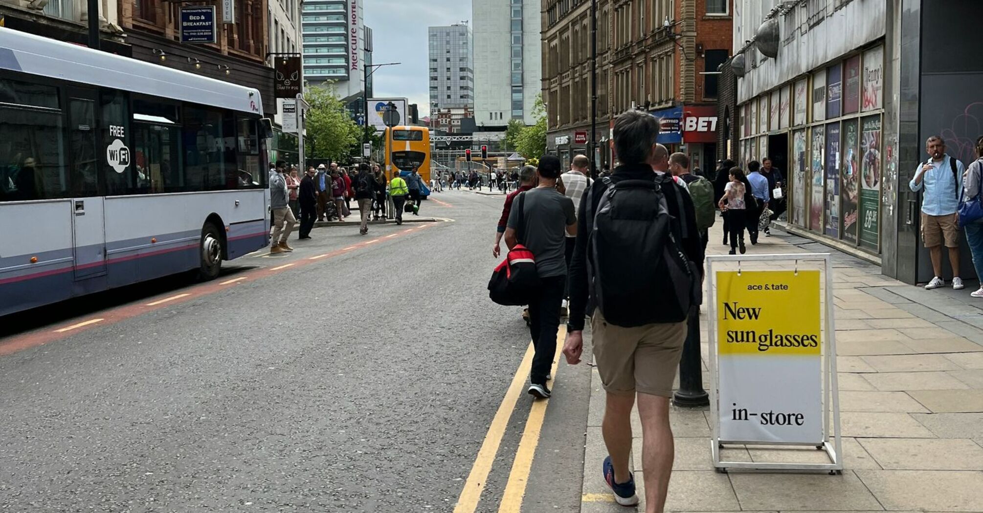 A busy street in Manchester with buses, pedestrians, and tall buildings under a cloudy sky