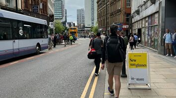 A busy street in Manchester with buses, pedestrians, and tall buildings under a cloudy sky