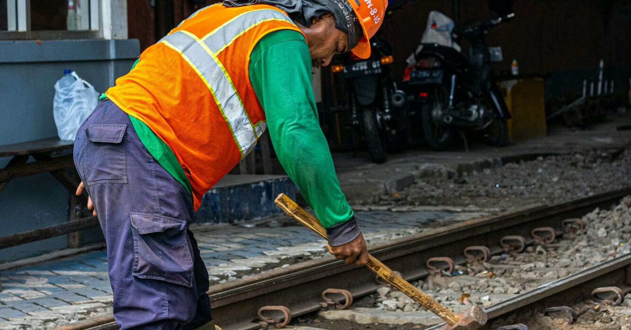 Construction worker in a safety vest and hard hat performing maintenance on railway tracks