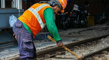 Construction worker in a safety vest and hard hat performing maintenance on railway tracks
