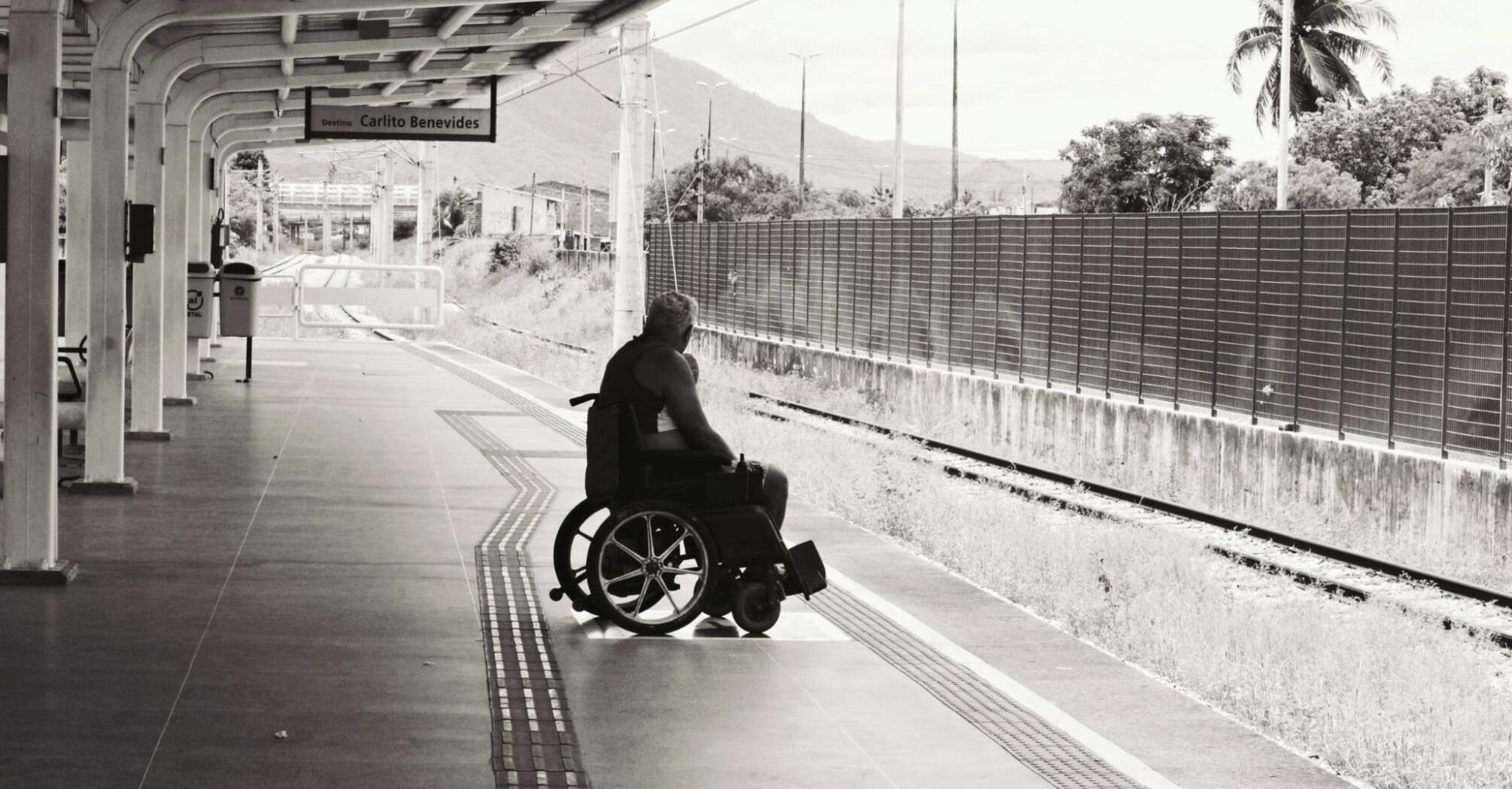 A man in a wheelchair waits alone on a train platform