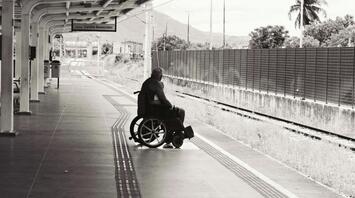 A man in a wheelchair waits alone on a train platform