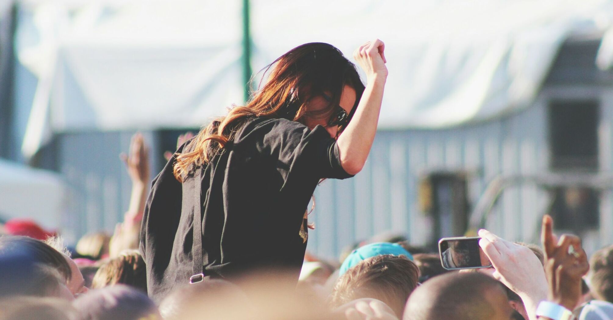 A person enjoying a music festival, seen from behind, surrounded by a crowd