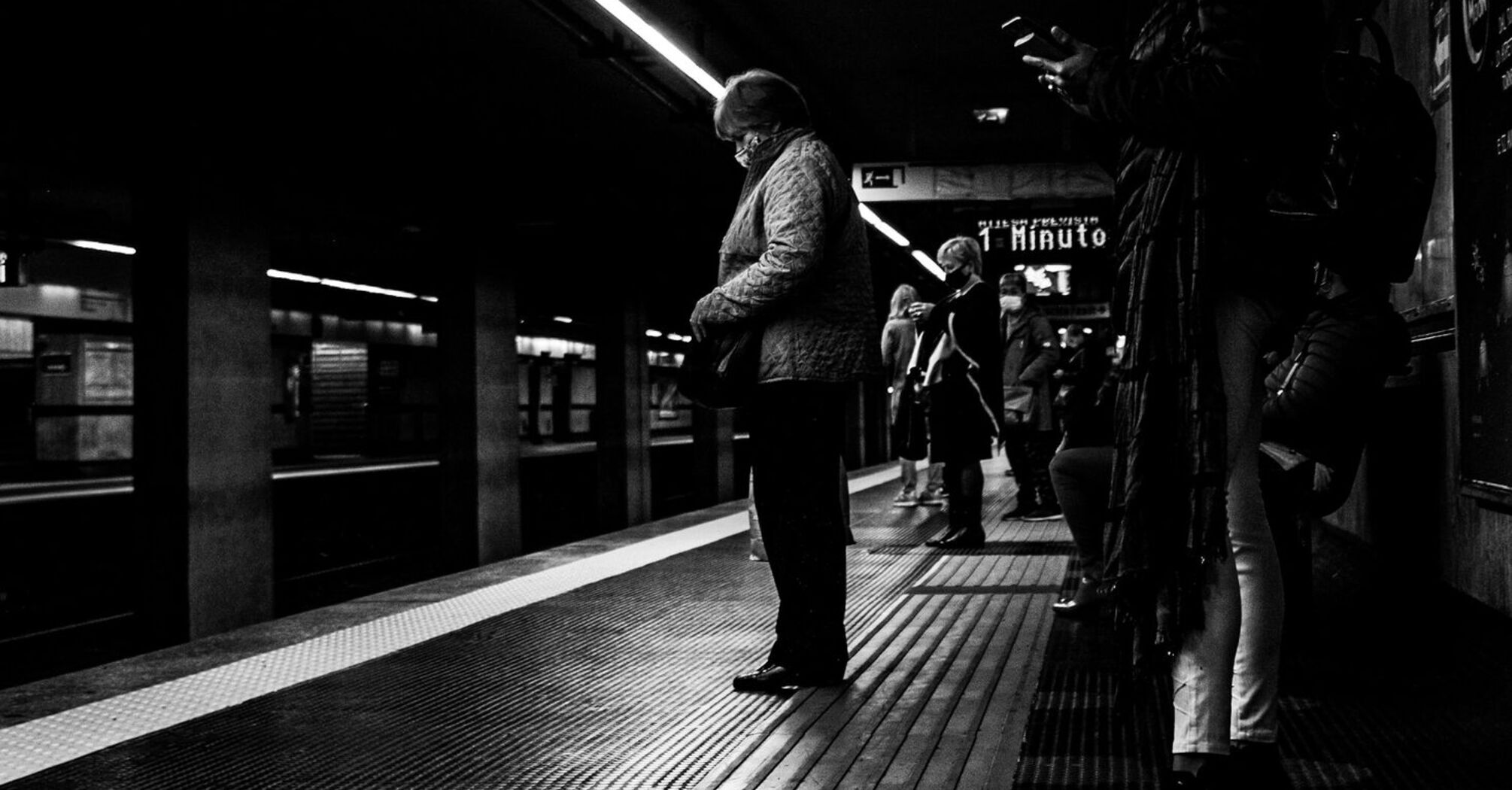 People waiting on a dimly lit train platform in Rome, captured in black and white