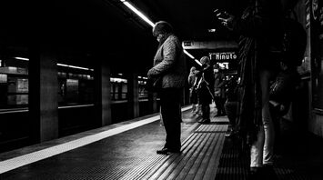 People waiting on a dimly lit train platform in Rome, captured in black and white