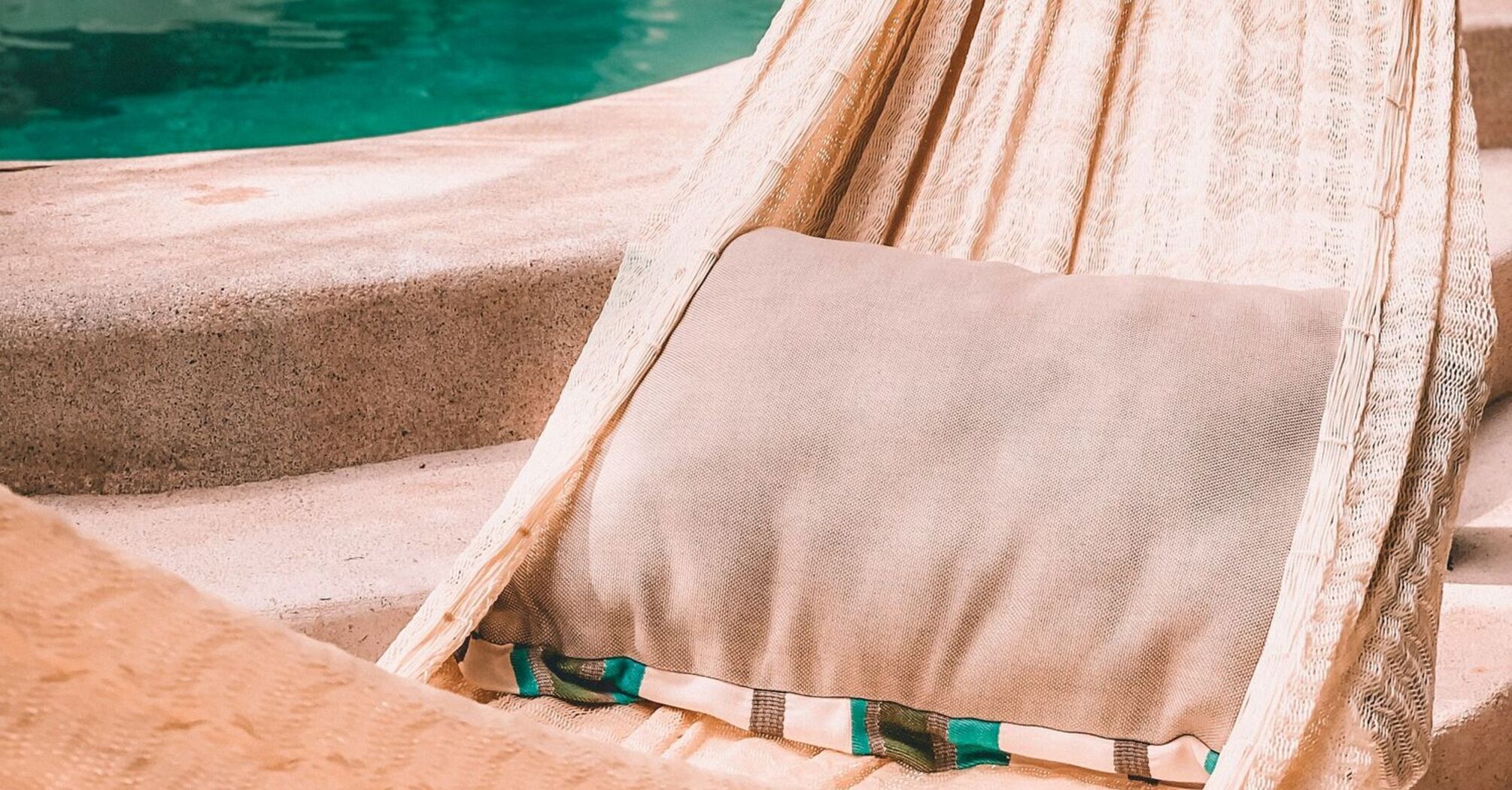 A hammock with a cushion hanging beside a serene pool in a tranquil, lush outdoor setting