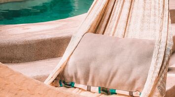A hammock with a cushion hanging beside a serene pool in a tranquil, lush outdoor setting