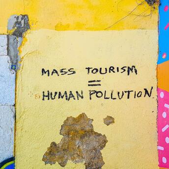 A graffiti on a yellow wall reading "Mass Tourism = Human Pollution," highlighting concerns over the impact of mass tourism