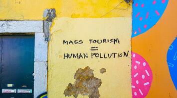 A graffiti on a yellow wall reading "Mass Tourism = Human Pollution," highlighting concerns over the impact of mass tourism