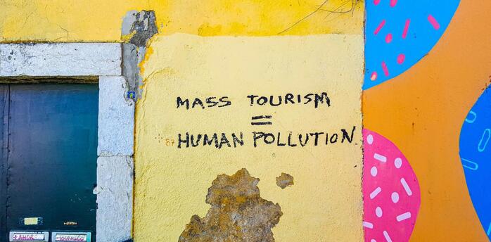 A graffiti on a yellow wall reading "Mass Tourism = Human Pollution," highlighting concerns over the impact of mass tourism