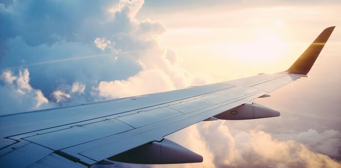 A view of an airplane wing flying above clouds during a bright and serene sunset