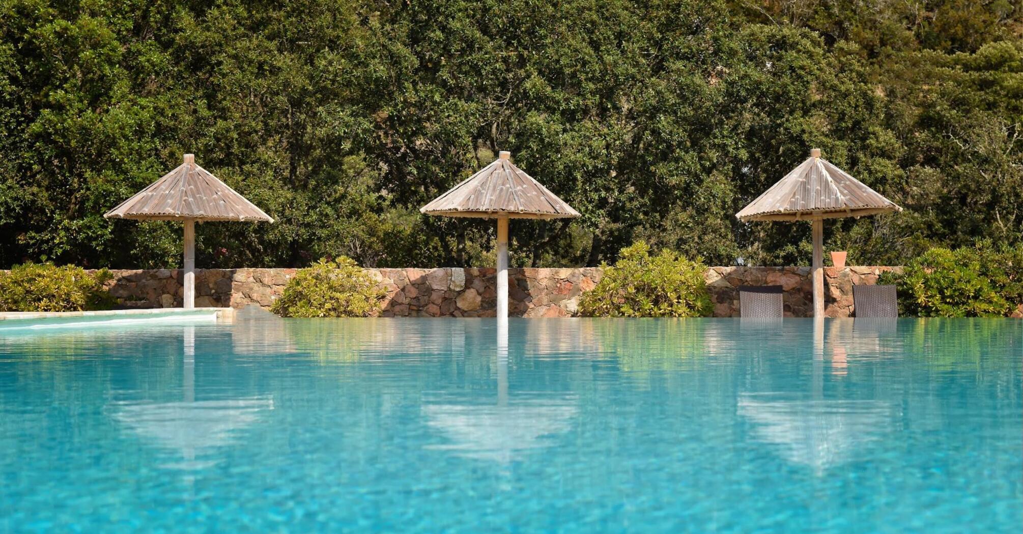 Three wooden umbrellas by a pool with a forest backdrop