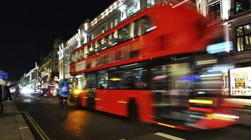 Blurred image of a red London double-decker bus speeding down a busy, illuminated street at night