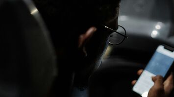 A young person holding onto a bus rail while looking at their phone