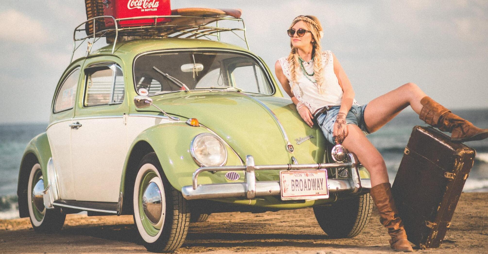 Woman relaxing on a retro car with suitcase by the sea