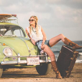 Woman relaxing on a retro car with suitcase by the sea