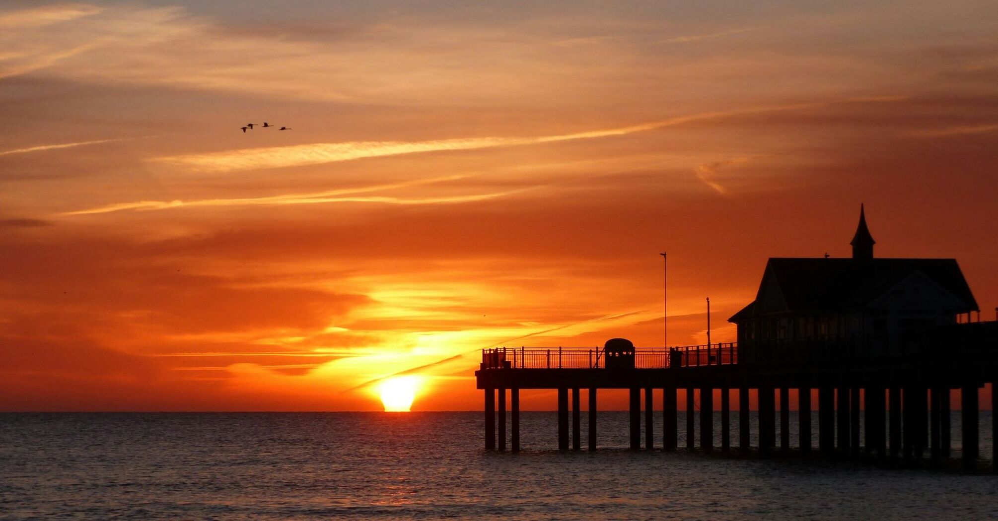 Sunset view over the ocean with a pier silhouette in Suffolk