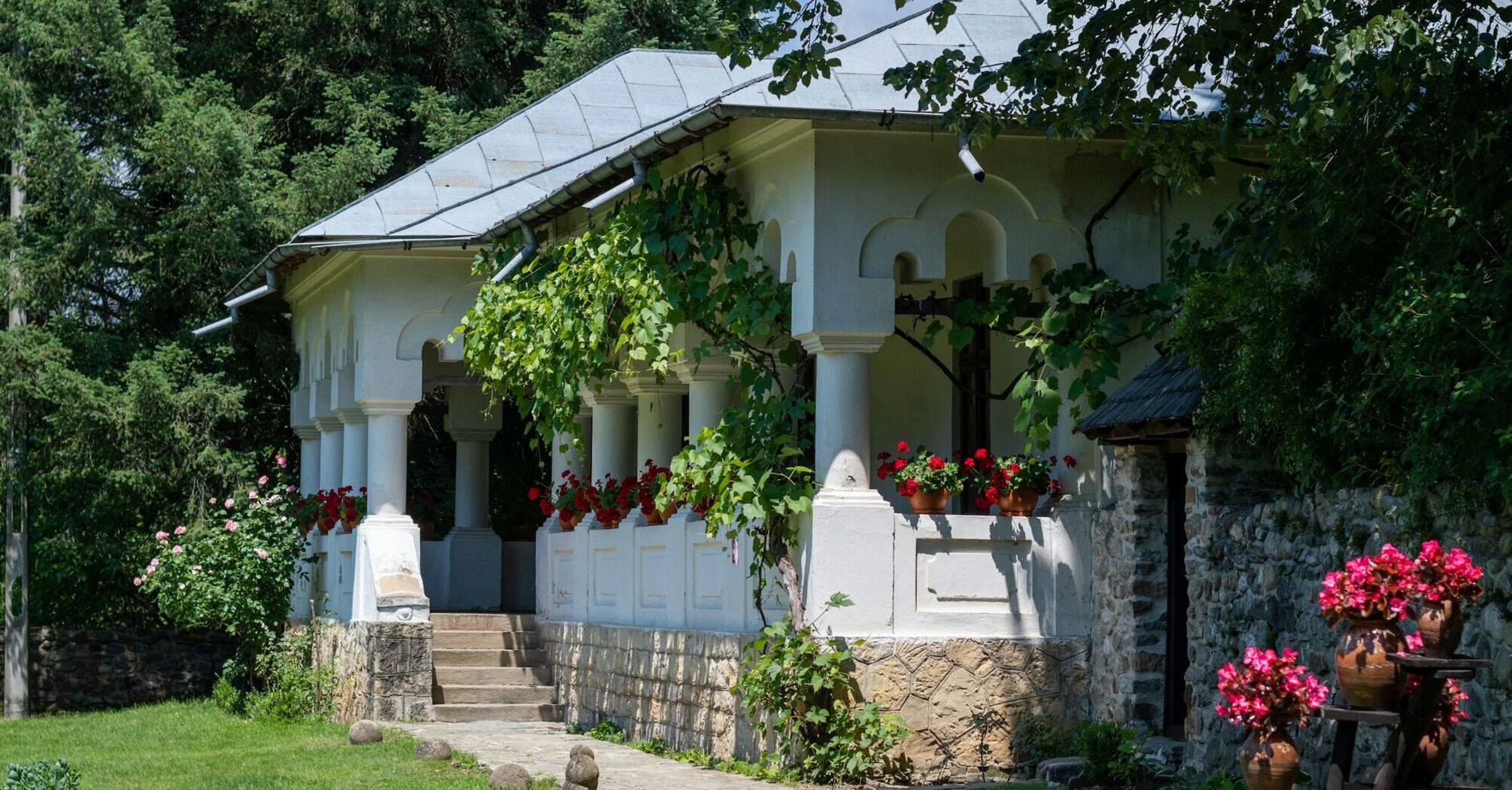 A beautiful traditional Romanian house with white walls, shingled roof, and vibrant red flowers in pots on the porch