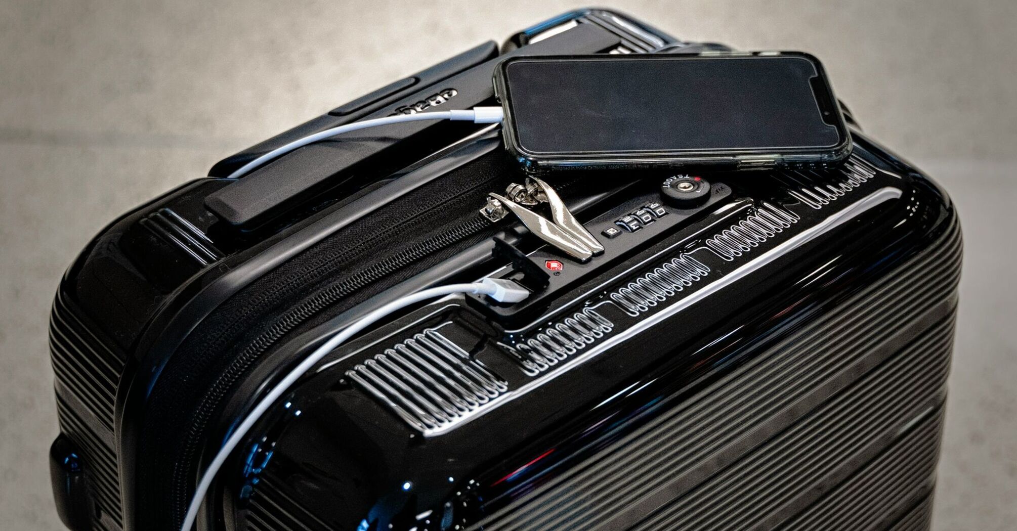 A black suitcase with a phone and charging cables on top