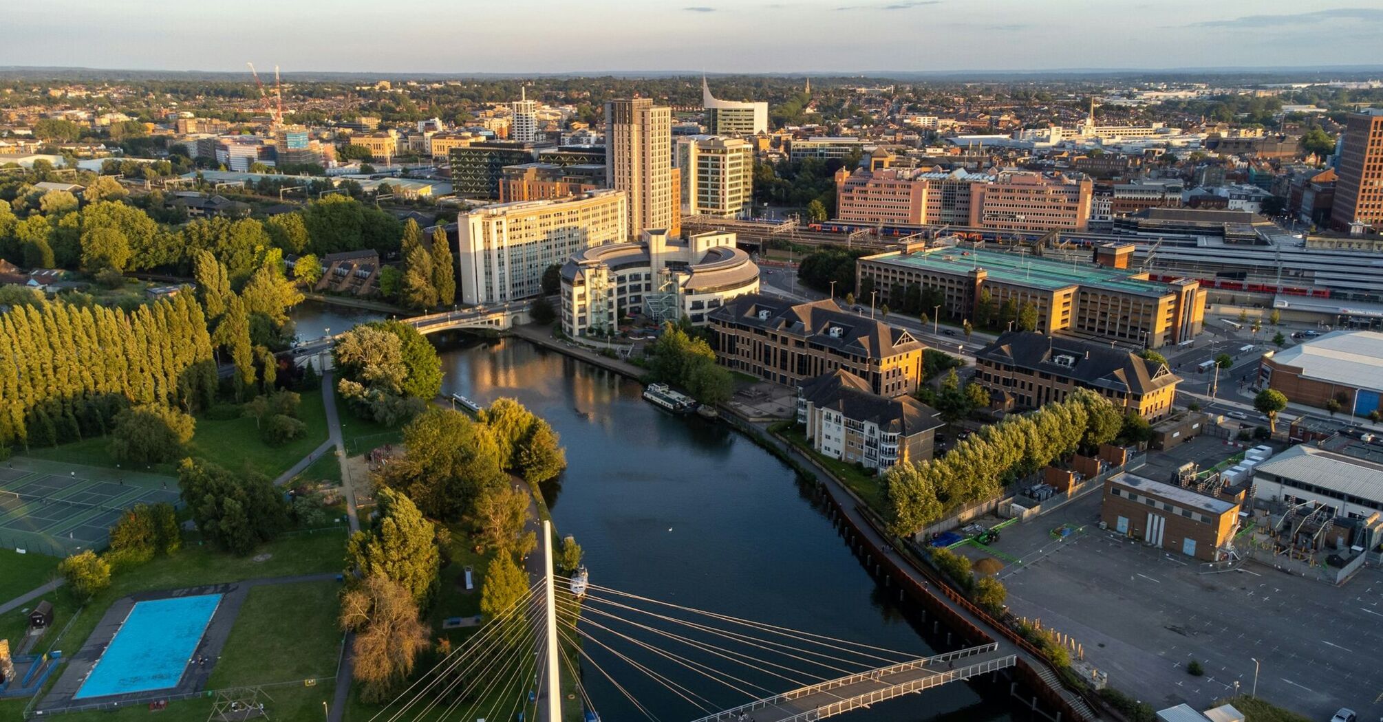 An aerial view of Reading, UK, showcasing modern buildings, a river, a bridge, and green spaces