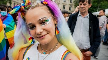 A young person with rainbow-colored hair and glitter makeup smiling at a Pride event