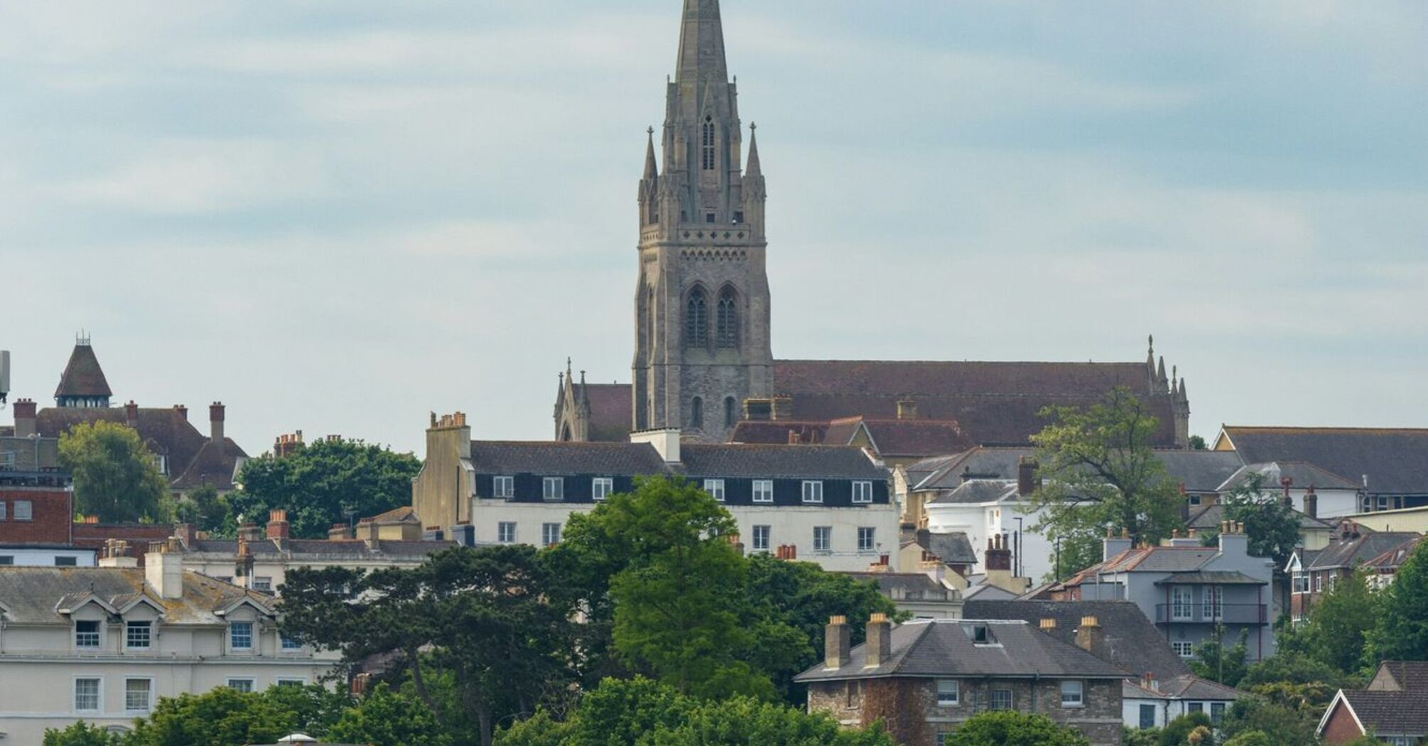 A view of Ryde on the Isle of Wight, featuring a prominent church spire and historic buildings surrounded by lush greenery, as seen from the water