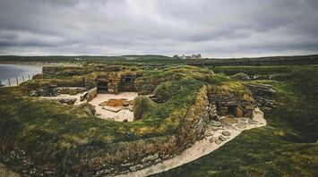 Ancient stone structures of Skara Brae in Orkney, with a cloudy sky and coastline in the background