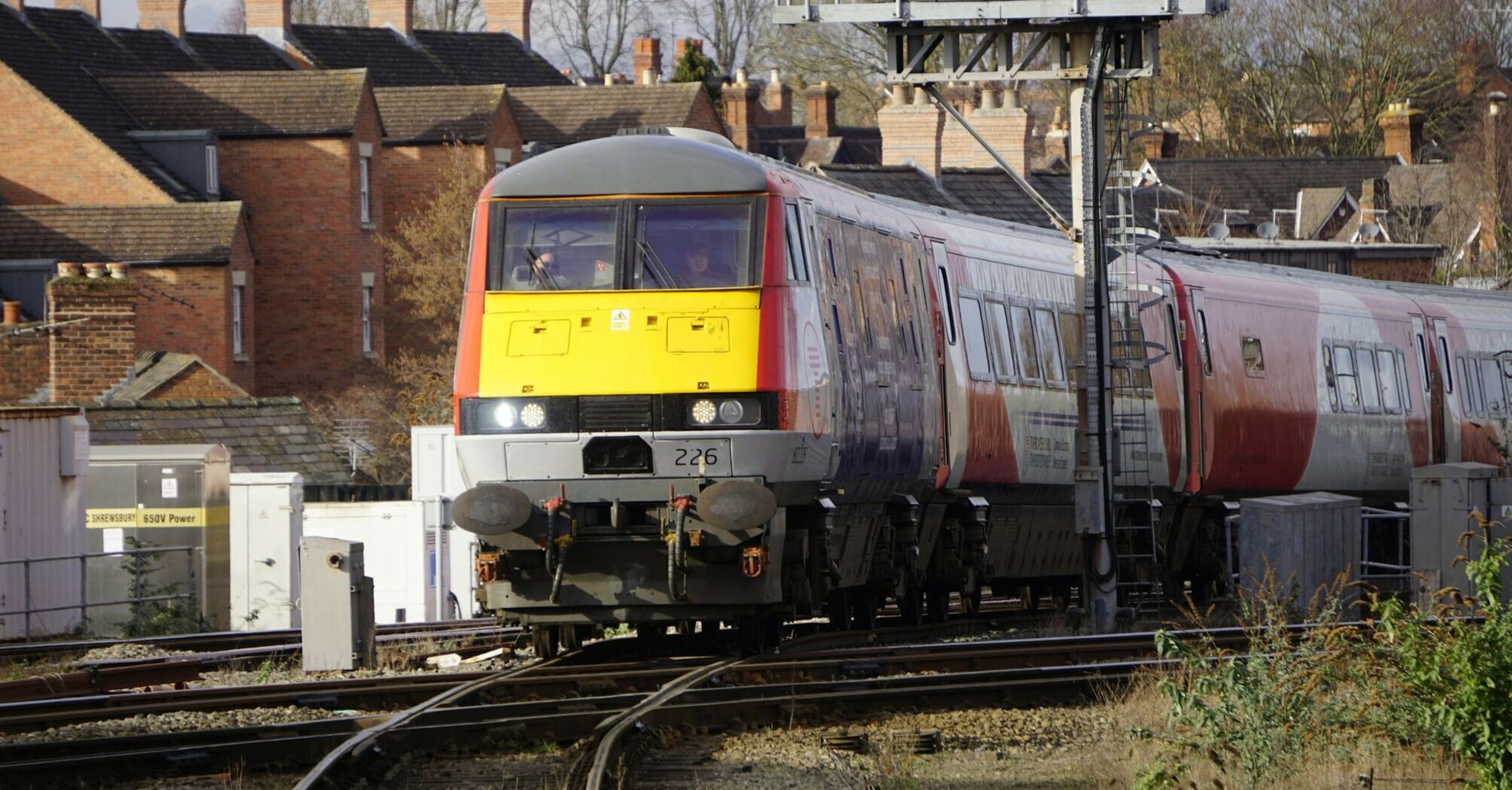 Transport for Wales train passing through a residential area with signal infrastructure