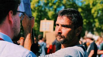 A man holding a sign engages in a serious conversation with another person during a protest