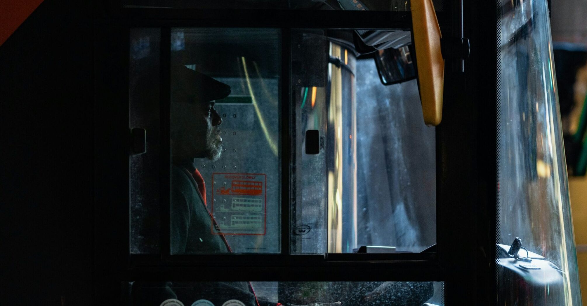 A bus driver in profile, seated in the driver's seat of a bus