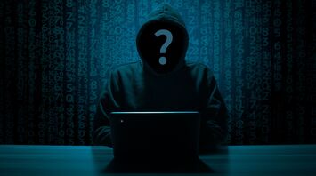 Anonymous hacker in a dark setting working on a laptop