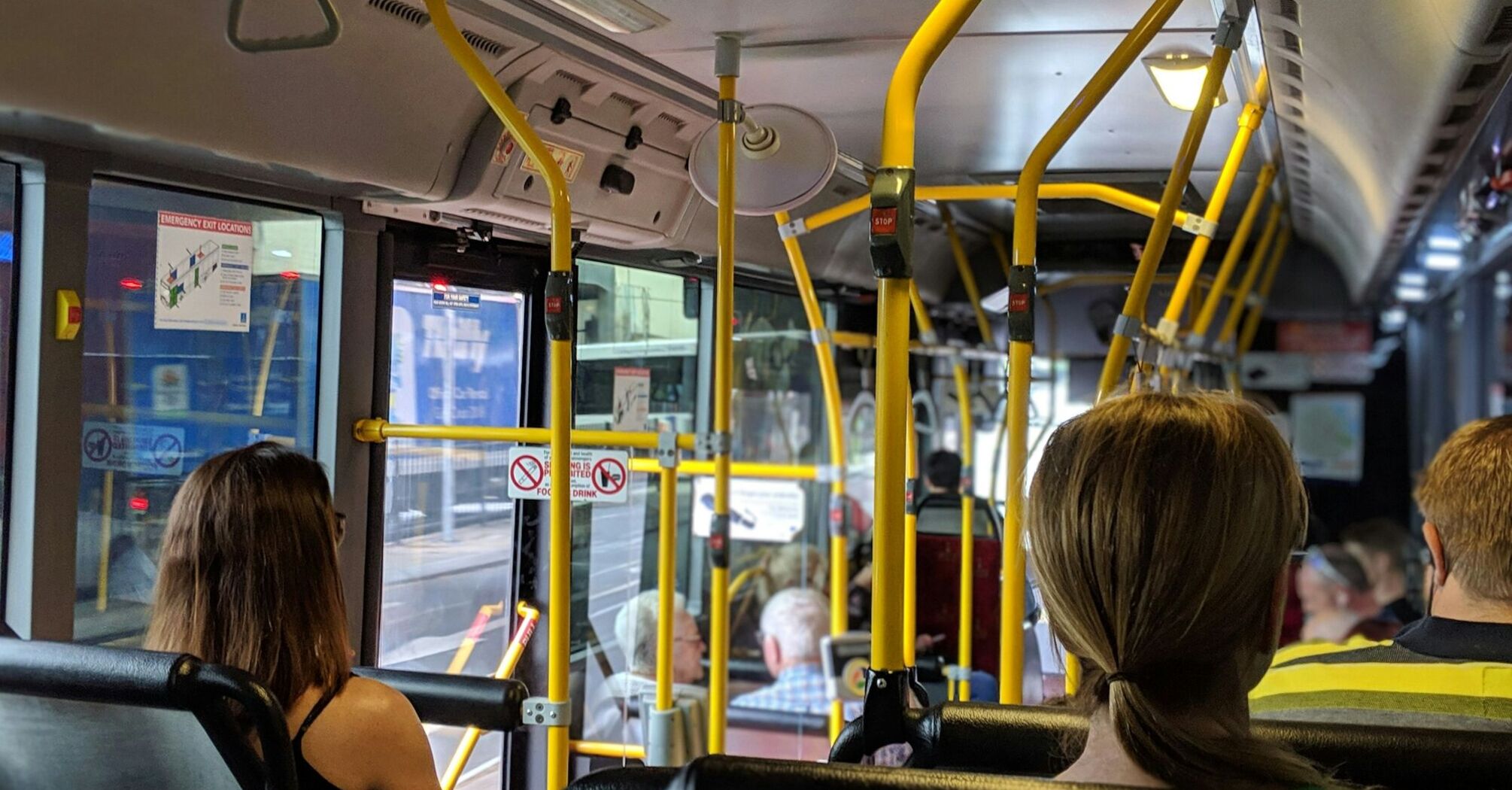 Passengers seated inside a bus with yellow handrails, traveling through a city