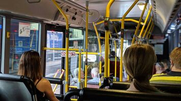 Passengers seated inside a bus with yellow handrails, traveling through a city