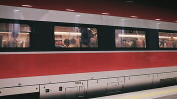 A red and white train carriage with passengers seated inside, captured at a station platform