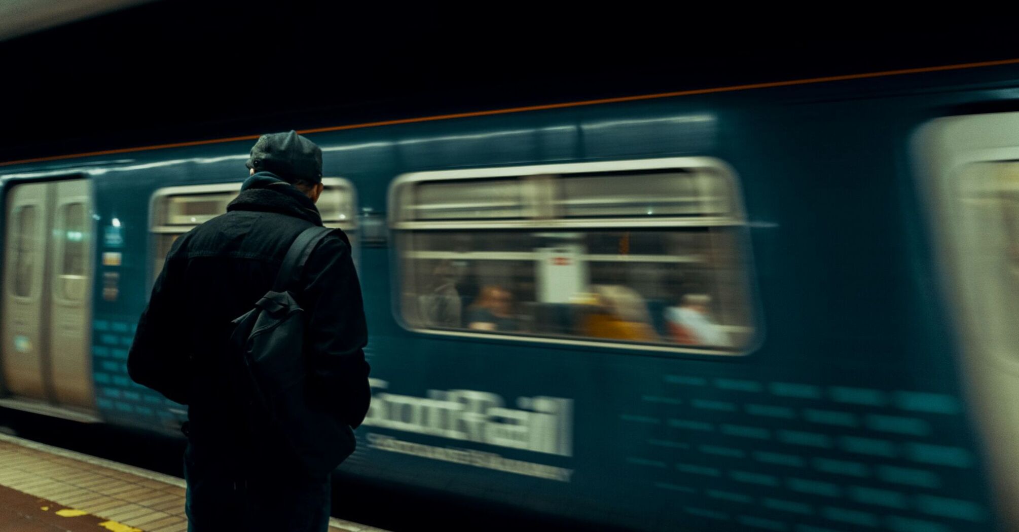 A person standing on a train platform, watching a passing ScotRail train