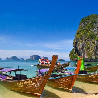 Traditional Thai longtail boats anchored by a scenic limestone cliff on a sunny day