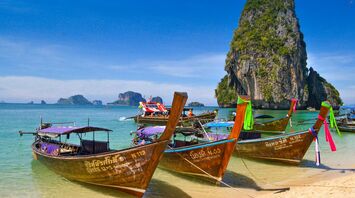 Traditional Thai longtail boats anchored by a scenic limestone cliff on a sunny day