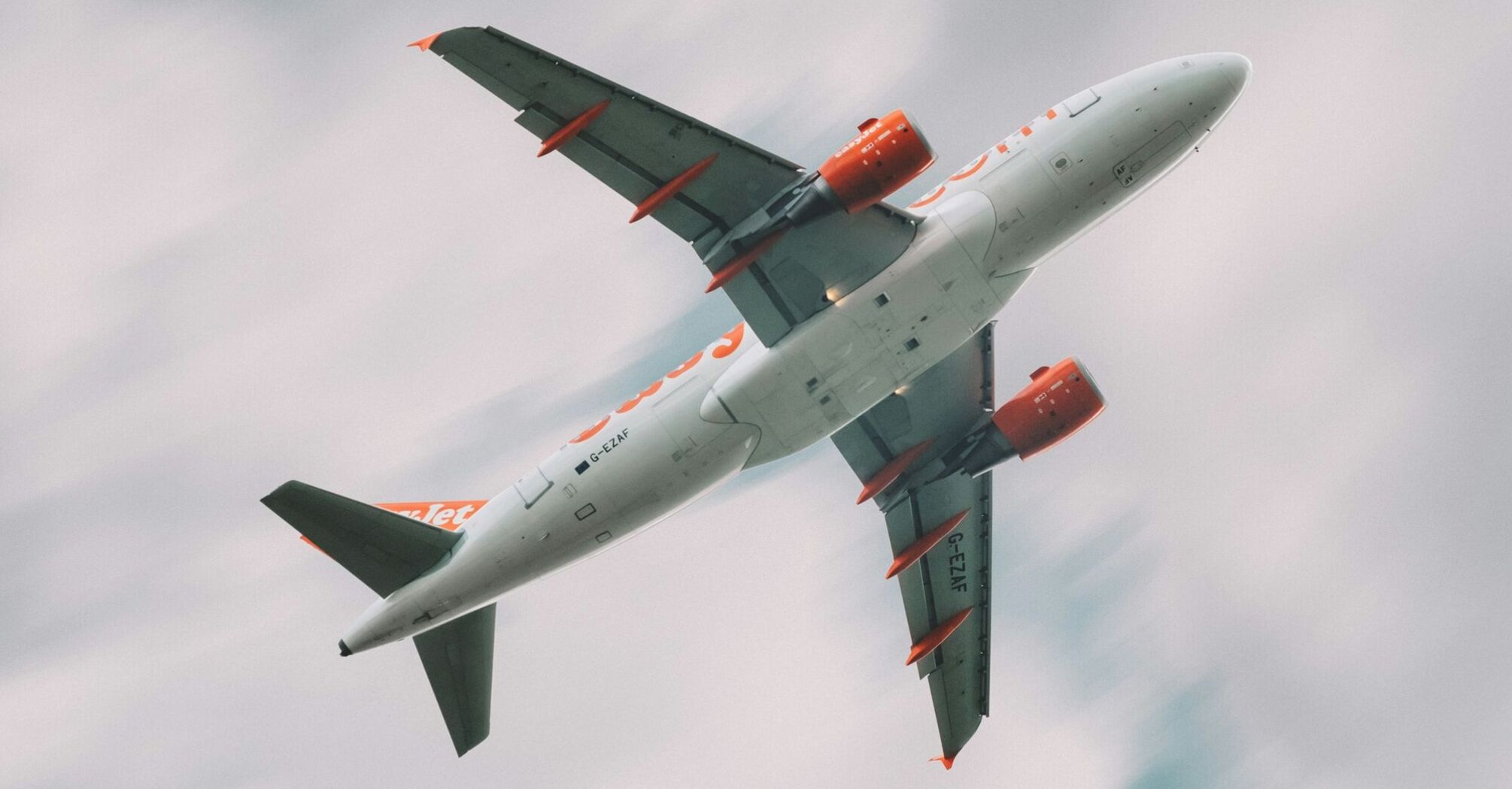 A low-angle shot of a easyJet airplane in flight with a cloudy sky background