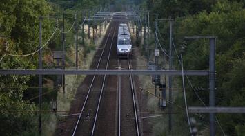 High-speed train moving on electrified railway tracks surrounded by greenery