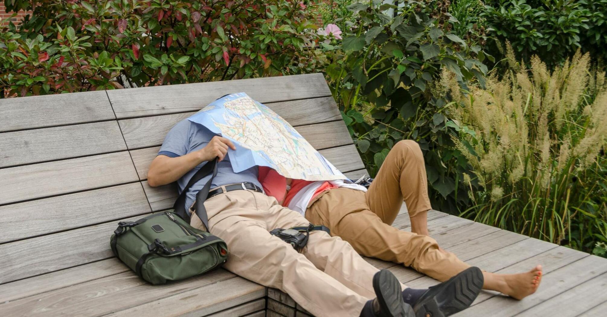 Couple resting on a bench with a map covering their faces