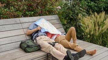 Couple resting on a bench with a map covering their faces
