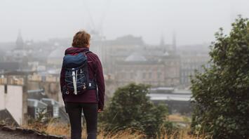 A person with a backpack stands on a hill, overlooking the misty skyline of Edinburgh