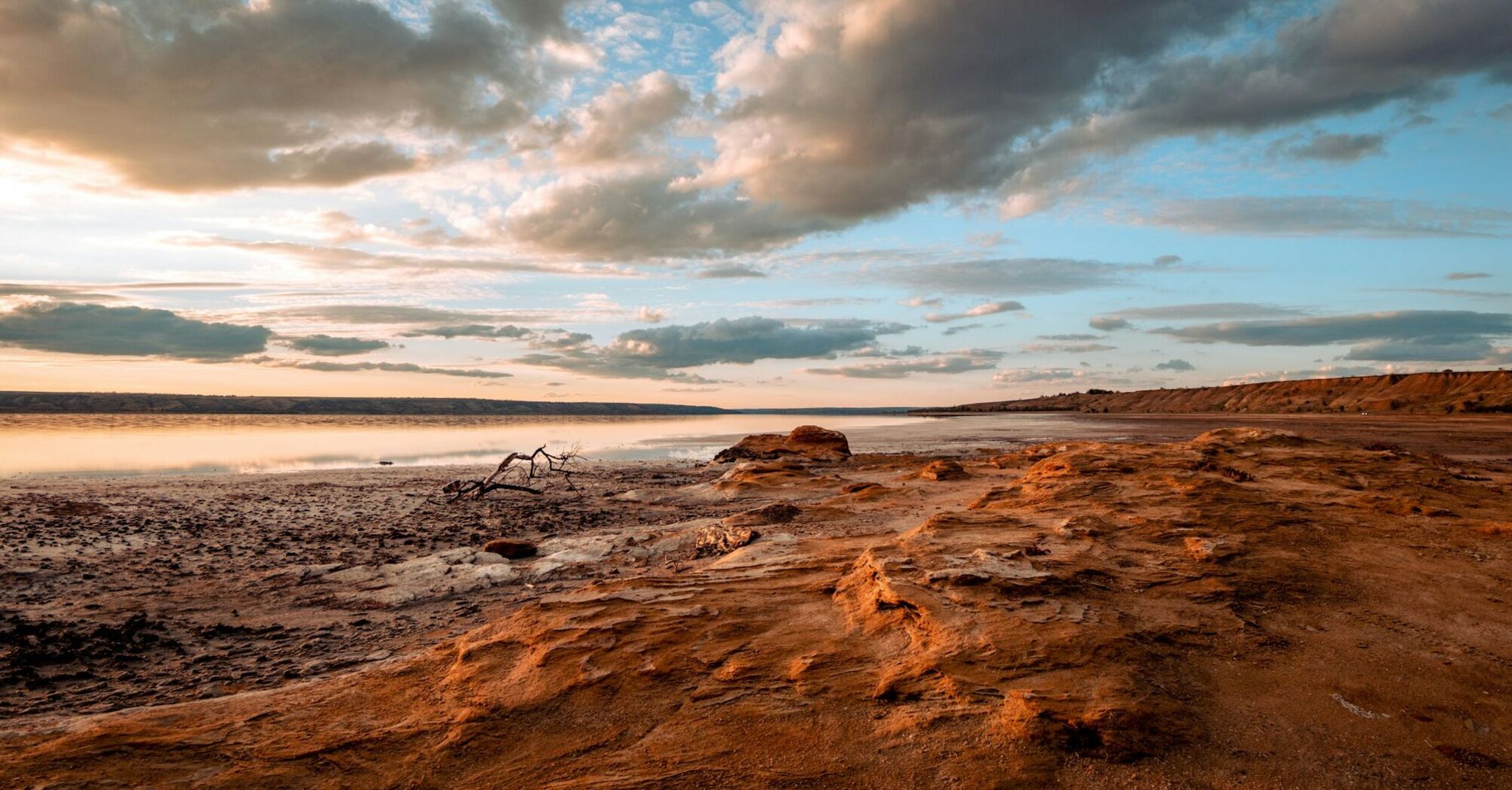 A dried-up lakeshore under a cloudy sky at sunset