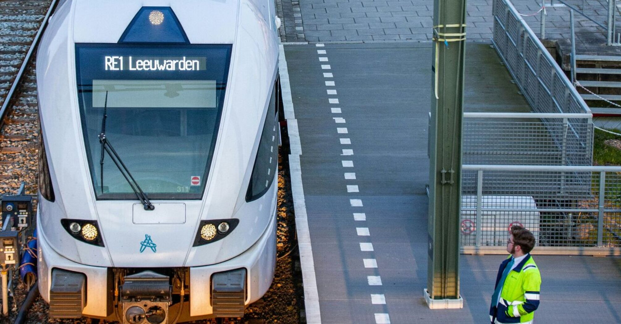 A modern Dutch train at a station platform, with a railway worker observing, preparing for departure