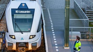A modern Dutch train at a station platform, with a railway worker observing, preparing for departure